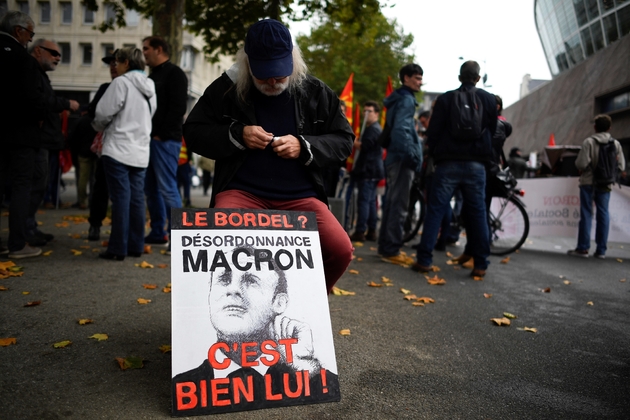 Un manifestant agenouillé près d'une pancarte dénonçant la politique sociale d'Emmanuel Macron, à Rennes, le 19 octobre 2017