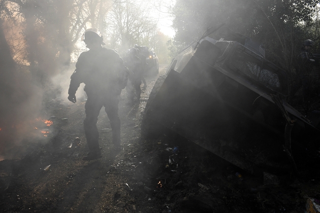 Des gendarmes marchent près d'un véhicule détérioré lors d'échauffourées avec les occupants de la ZAD de Notre-Dame-des-Landes, le 13 avril 2018