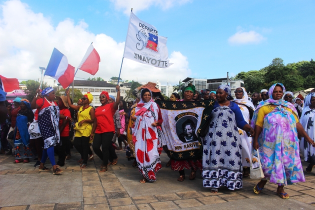 Dans le cortège, en garde partie composé de mahoraises portant le salouva, flottaient de nombreux drapeaux français, européens, ou siglés 