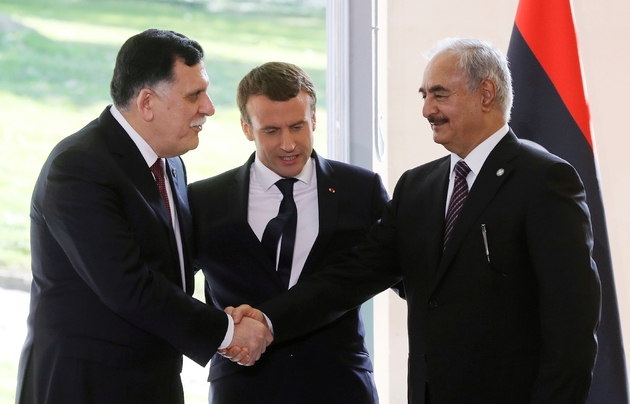 le Premier ministre libyen Fayez al-Sarraj (g) et le maréchal Khalifa Haftar (d), l'homme fort de l'est libyen, se serrent la main en présence du président Emmanuel Maron, le 25 juillet 2017 à la Celle-Saint-Cloud, près de Paris