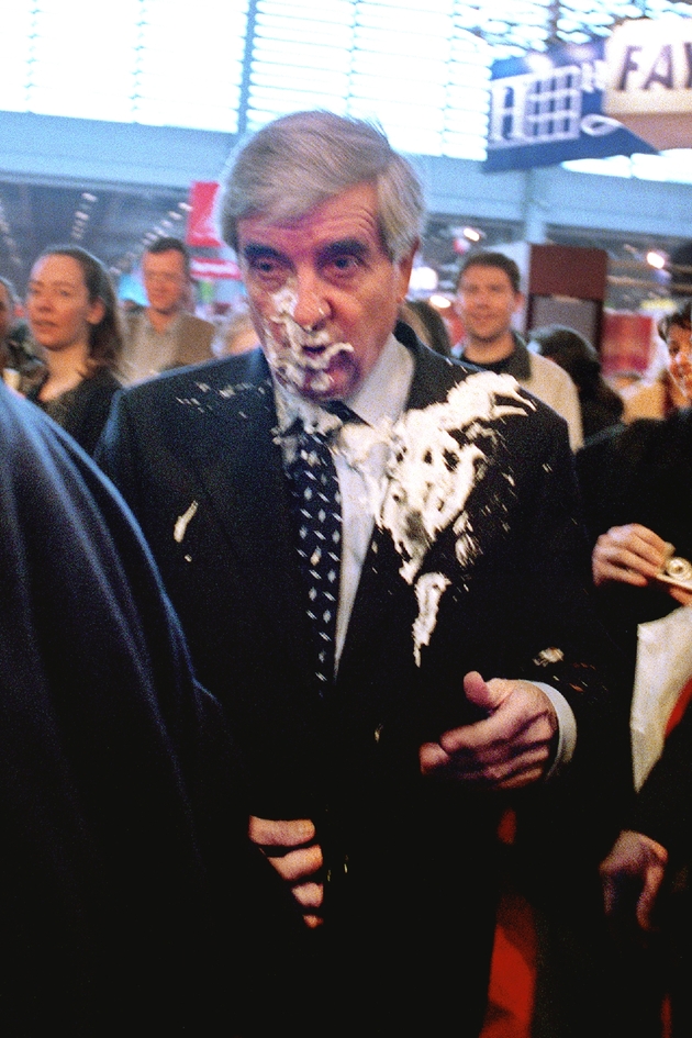 Le candidat du Pôle Républicain à l'élection présidentielle Jean-Pierre Chevènement (C), baisse la tête, le 24 mars 2002 à Paris au salon du livre après avoir reçu au visage une tarte à l'ananas lancée par 