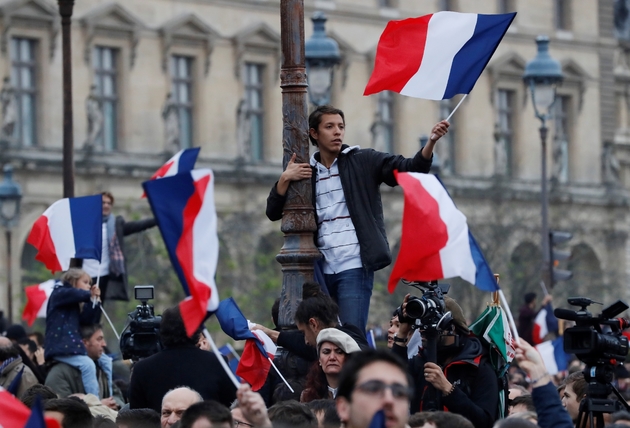 Des militants montés sur des lampadaires et des feux rouges agitent des drapeaux, le 7 mai 2017 sur l'esplanade du musée du Louvre à Paris