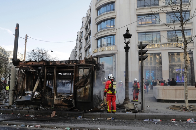 Des pompiers près d'un kiosque à journaux incendié lors de la manifestation des 